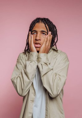 Genç bir adamın portresi kaygısını yüzünü tutarak ifade eder. Pembe arka plandaki endişenin ağırlığını somutlaştırır.