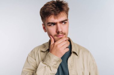 Düşünceli bir gencin portresi, beyaz arka planda derin bir tefekkür içinde, çenesini elinde tutar.