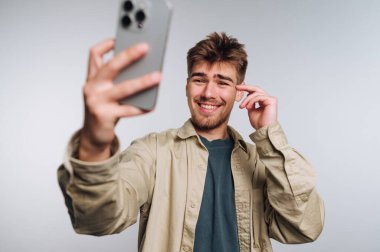 Genç adamın portresi düşünürken gülümsüyor, akıllı telefonuna bakıyor, bu da beyaz arka planda tefekkür ve yansıtıcı neşe olduğunu gösteriyor.