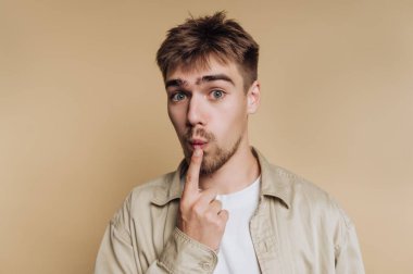 Genç bir adamın portresi parmağını dudaklarına koyuyor. Stüdyonun minimalist arka planında sessizlik ve gizliliği simgeliyor..