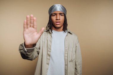 Ciddi bir ifadeyle genç bir adamın portresi elini kaldırıyor, bej arka planda açıkça reddediyor ya da anlaşmazlık çıkarıyor.