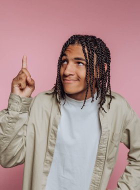 Genç bir adamın portresi, pembe arka planda eğlence ve yaratıcılığı temsil eden arsız bir gülümsemeyle bir parmağını kaldırır.