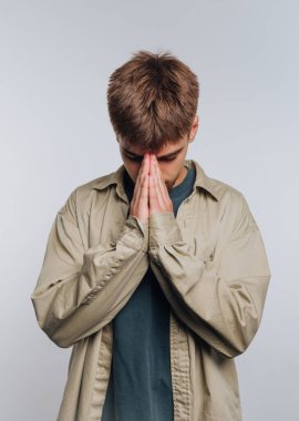 Genç bir adamın portresi, elleri duada birbirine bastırılmış bir şekilde başını eğiyor, bir yansıma anını simgeliyor ve beyaz arka planda iç huzuru arıyor.