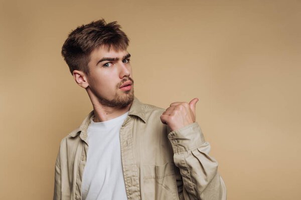 портрет молодого человека демонстрирует любопытное выражение, глядя боком на бежевый фон