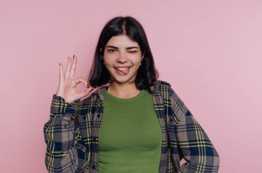 Pembe bir duvarın önünde duran genç bir kadın, eliyle 