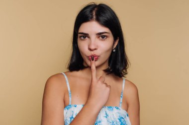 Genç bir kadın, eğlence ve gizem hissi veren parmaklarıyla şakacı bir şekilde poz veriyor. Açık mavi bir elbise giyiyor ve kendine güvenen bir gülümsemesi var..