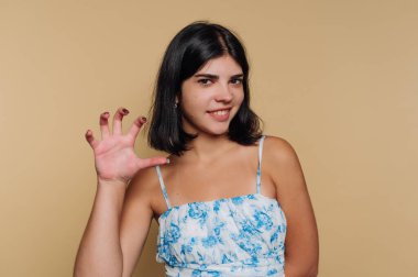 Omuz hizasında koyu saçlı genç bir kadın tek eliyle pençe gibi bir jest yaparken muzip bir şekilde gülümsüyor. Renkli desenli bir bluz giyiyor. Bu da onun oyunculuğuna çekicilik katıyor..