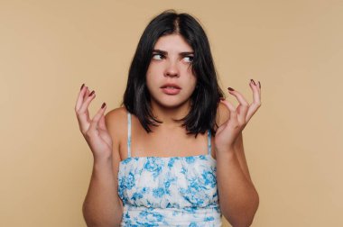 Genç bir kadın evde dikilirken hayal kırıklığı belirtileri gösterir. Mavi çiçekli bir bluz giyiyor ve koyu renk saçları var. Tarafsız arka plan, öğleden sonra ışığında ifadesini canlı bir şekilde vurguluyor..