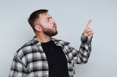 Sakallı ve ekose gömlekli bir adam yukarıyı göstererek şaşkınlığını gösterir. Sade bir arka planı olan kapalı bir yerde. Bu da gündüzleri sıradan bir atmosfer olduğunu gösteriyor..