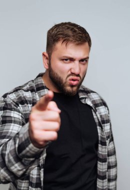 Ekose gömlek giyen bir adam parmağını gösterirken ciddi bir yüz ifadesi sergiler. Duruşu önemli bir konuşma yaptığını ya da önemli bir noktaya parmak bastığını gösteriyor..