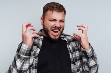 Bir adam yüzündeki ifadeyle hayal kırıklığını belli eder, elleri öfke jesti ile havaya kalkar. Kareli bir tişört ve siyah bir tişört giyer..