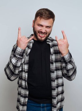 Neşeli genç bir adam elleri havada poz verir. Siyah bir tişörtün üzerine ekose bir gömlek giyiyor ve neşeli bir gülümseme sergiliyor, canlı ruhunu kapalı bir ortamda sergiliyor.