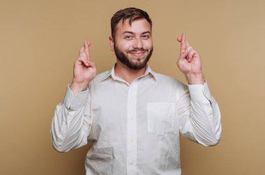 Genç bir adam, şans getirmesi için şans dileyerek, bir tebessümle güvenle ayakta duruyor. Arka planda, olumlu havayı arttıran yumuşak ve sıcak bir ton var..