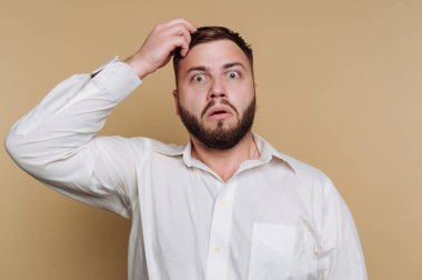 Şaşkın şaşkın bakan bir adam kafasını karıştırıyor. Tepkisi, tarafsız bir arkaplanda güvensizlik ya da şok olduğunu gösteriyor. Sahne, bir şeyin farkına varma anıdır..