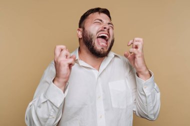 Elleri sıkılmış, ağzı açık bir şekilde çığlık atan bir adam büyük bir hayal kırıklığı yaşar. O, basit bir bej arka plan karşısında beyaz bir gömlek giyer, duyguyu vurgular.