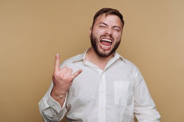 Sakallı genç bir adam neşeli bir şekilde rock 'n roll hareketi yapıyor. Enerjisini ve coşkusunu, tarafsız bir arkaplan karşısında sergiliyor..