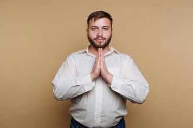 Minnettarlığımızı göstermek için ellerimizi birleştirelim. Beyaz bir gömlek giyiyor ve iyi bakımlı bir sakalı var. Arkaplan nötr bir renktir, sakin bir atmosfer yaratır..