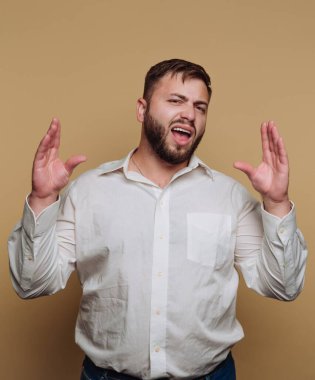 Bir adam kendine güvenerek ayakta duruyor, şarkı söylerken ya da konuşurken kendini ifade ediyor. Açık renkli bir gömlek giyiyor ve enerjisini vurgulayan tarafsız bir arka planla performansında tutku gösteriyor..