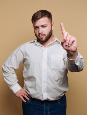 Bir adam, bir parmağı havada, rahat bir beyaz gömlek ve kot pantolon giyiyor. Tarafsız bir zemine karşı cesur bir duruş sergiliyor, güvenilirliğini ifade ediyor..