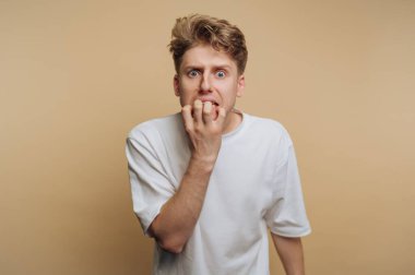 Genç bir adam bir elmayı ısırırken şok olmuş bir ifadeyle tasvir edilir. Saçı dağınık ve düz beyaz bir gömlek giyiyor. Arka plan bej renginde, sakin bir atmosfer yaratıyor..