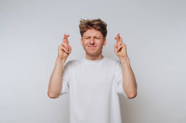 Genç bir adam arka planda duruyor, parmaklarını çapraz yapıyor ve umutlu bir ifadeyle gözlerini kapıyor. Sahne beklenti ve heyecan verir..