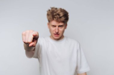 Genç bir adam düz bir arkaplan karşısında duruyor, ciddi bir ifadeyle ileri bakıyor. Jesti güçlü duygular taşıyor, izleyiciyle bağlantı kuruyor..