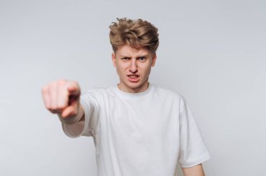 Sarışın, dağınık saçlı genç bir adam gözle görülür bir öfke ve hayal kırıklığı sergiliyor. Tarafsız bir arkaplana karşı güçlü bir ifade ya da argüman sergiliyormuş gibi ileri doğru işaret ediyor..