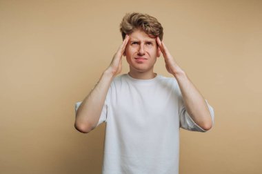 Genç bir adam elleri başının üstünde duruyor, hayal kırıklığı belirtileri gösteriyor. İfadesi bunaltıcı bir his veriyor. Basit arka plan duygularını vurguluyor..