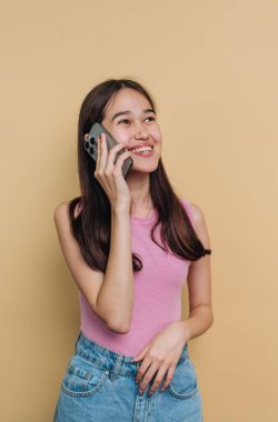 Uzun saçlı neşeli genç bir kadın açık sarı bir duvarın önünde dururken telefonla konuşmaktan zevk alıyor. Pembe bluz ve kot şort giyiyor, pozitif enerji yayıyor..