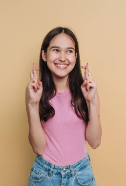 Genç bir kız şans dilemek için şans dileyen neşeli bir ifadeyle ayakta duruyor. Pembe bir bluz ve kot şort giyiyor, güneşli sarı bir fonda poz veriyor..