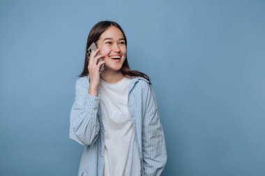 Mavi arka planda akıllı telefonla konuşurken gülümseyen genç bir kadın..