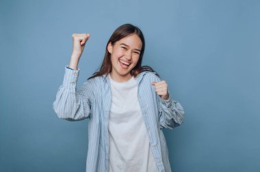 Mavi arka planda neşeli bir ifadeyle kutlama yapan genç bir kadın..