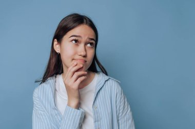 Mavi arka planda düşünceli bir duruş sergileyen genç bayan..