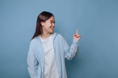 Gülümseyen ve mavi arka plana işaret eden genç bir kadın..