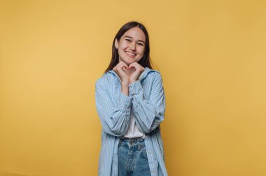 Gülümseyen kadın, sarı arka planda elleri olan kalp şekli yaratıyor..