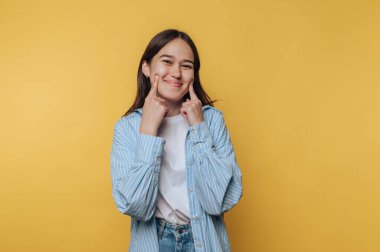 Gülümseyen ve yanaklarını sarı arka plana gösteren genç bir kadın..