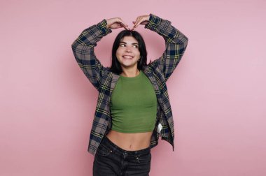 Gündelik kıyafetli genç bir kadın elleriyle kalp şekli yapıyor..