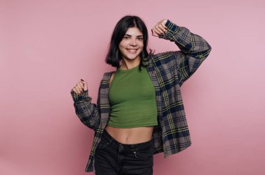 Pembe arka planda poz veren sıradan giyinmiş genç bir kadın..