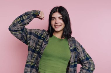 Ekose gömlekli genç bir kadın pembe bir arka plana karşı güvenle gülümsüyor..