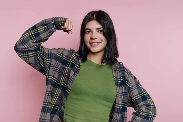Ekose gömlekli genç bir kadın pembe bir arka plana karşı güvenle gülümsüyor..