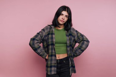 Pembe arka planda poz veren sıradan giyinmiş genç bir kadın..