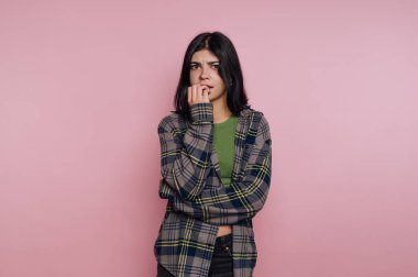 Pembe arka planda tırnaklarını yiyen endişeli bir kadın..