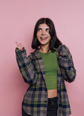 Gülümseyen kadın, ekose gömlekli, pembe arka plana yan bakan..