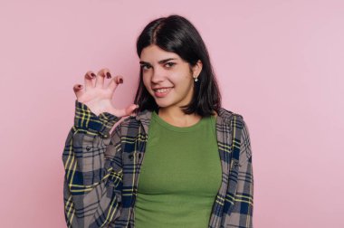 Genç bir kadın pembe arka planda bir pençe hareketi yapıyor.