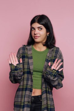 Şüpheli bir ifadesi olan, ekose gömlek giyen ve pembe arka planda yeşil bluz giyen bir kadın..