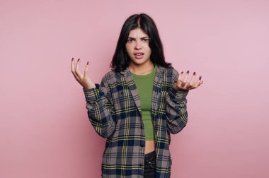 Kafası karışmış, ekose gömlek giymiş, pembe arka planı olan genç bir kadın..