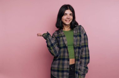 Ekose gömlekli gülümseyen kadın pembe arka planda el kol hareketi yapıyor..