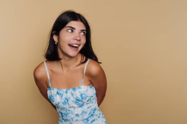 Çiçekli elbiseli genç bir kadın bej bir arka plana gülümsüyor..