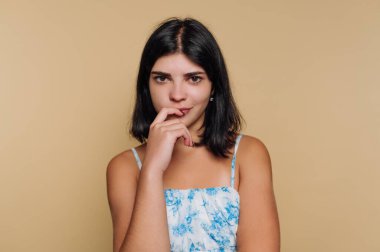 Bej arkaplana karşı düşünceli bir ifade takınan genç kadın..