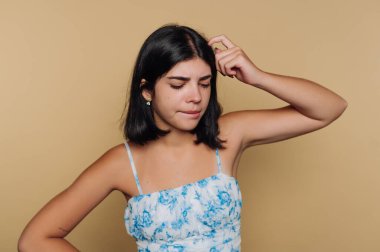 Çiçekli elbiseli, başını kaşıyan, kafası karışmış genç bir kadın..